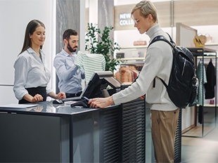 Kunde an der Kasse im Einzelhandelsgeschäft, der eine Zahlung mit einer Karte durchführt, während das Personal Kassensysteme nutzt.